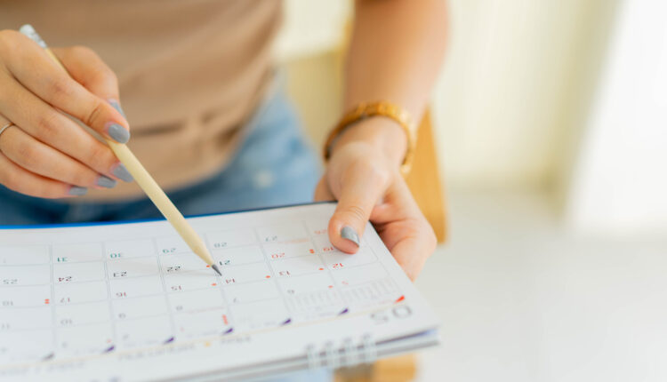 close up on senior employee woman hand using pen to writing schedule on calendar to make appointment meeting or manage timetable each day at house for work from home concept